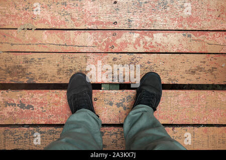 Pieds masculins en noir sneakers position sur grungy red parquet au sol, vue à la première personne Banque D'Images