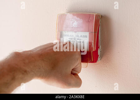 Poing mâle se casse le couvercle en plastique d'un bouton d'alarme incendie, la photo en gros plan avec selective focus Banque D'Images