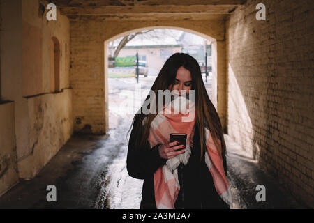 Young woman using smart phone tout en marchant à travers la ville pendant l'hiver en Banque D'Images