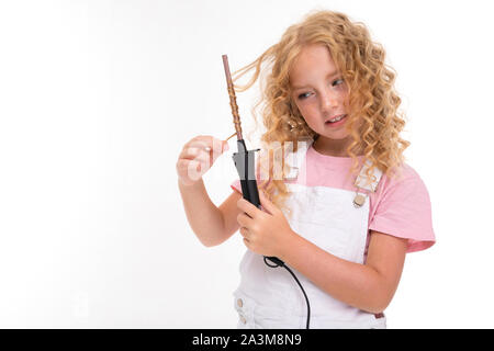 Une petite fille aux cheveux rouges heap dans un pyjama blanc, jersey, blanc sneakers tourne ses cheveux sur une fine la charrue. Banque D'Images