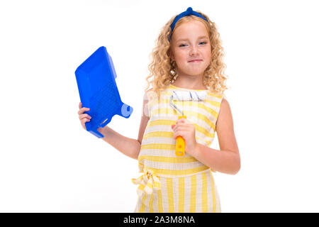 Une petite fille aux cheveux rouges heap dans un livre blanc et jaune costume d'été à rayures bleu, avec un bandage sur la tête avec un rouleau de peinture murale. Banque D'Images