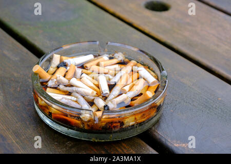 Le cendrier plein de mégots de cigarettes sur une table après la pluie Banque D'Images