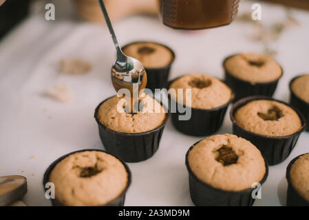 Le Baker crée des cupcakes dans des moules. Biscuits de remplissage avec du caramel liquide. Banque D'Images