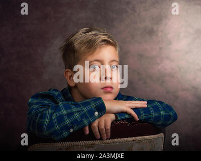 Beau petit garçon, blond, triste, appuyé sur une chaise Banque D'Images