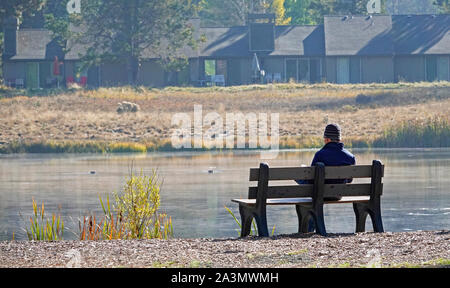 Un homme est assis sur un banc tranquille le long d'une rivière misty tôt le matin, la lecture d'un magazine, dans le centre de l'Oregon. Banque D'Images