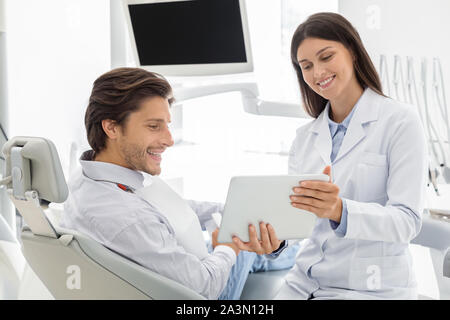 Cheerful dentist showing patient Résultats du traitement sur la tablette numérique Banque D'Images