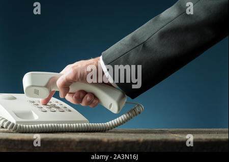 Main d'un businessman holding combiné de téléphone de composer le numéro de téléphone sur blanc téléphone fixe. Sur fond bleu marine. Banque D'Images