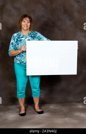Shot vertical d'un friendly middle-aged woman holding a blank sign sur un fond brun. Banque D'Images
