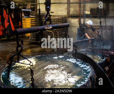 Deux bacs d'immersion ronds remplis d'eau fumante se trouvent dans la salle de cuisson de l'usine Kanesa katsuobushi, un ouvrier portant un foulard blanc guidant le panier métallique sur le palan à chaîne dans le deuxième bac en arrière-plan. Nishiizu-Cho, préfecture de Shizuoka, Japon. Banque D'Images