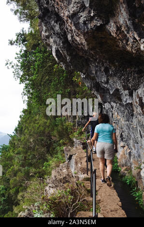 Les gens qui marchent sur un chemin étroit sur le bord de la roche au cours de Levada do Caldeirao Verde Trail. Les rochers et les arbres verts. Randonnée, trekking dangereuses. Attraction touristique portugaise. Banque D'Images