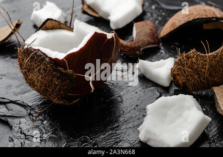 Noix de coco biologique avec des morceaux hlf sur fond noir en ardoise noire. Aliments à forte teneur en gras sain concept. Banque D'Images