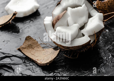 Noix de coco biologique avec des morceaux hlf sur fond noir en ardoise noire. Aliments à forte teneur en gras sain concept. Banque D'Images