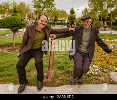 Isfahan, Iran - 2019-04-12 - deux hommes assis sur une clôture de la chaîne de prendre un moment de leur conversation à sourire pour le photographe à l'étranger. Banque D'Images