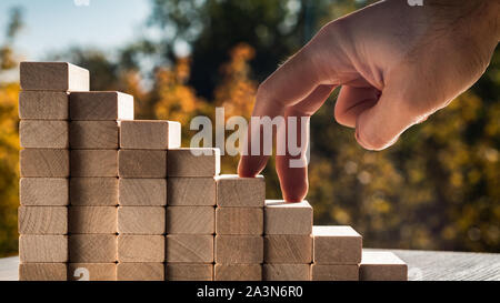 Concept de promotion de l'entreprise objectifs. Les doigts de l'homme monter les escaliers faits de blocs de bois contre l'arrière-plan de feuilles d'automne sur une journée ensoleillée. Banque D'Images