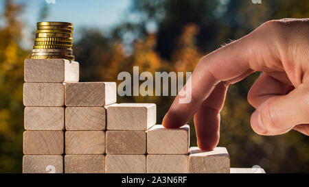 Concept de promotion de l'entreprise objectifs. Les doigts de l'homme monter les escaliers faits de blocs de bois contre l'arrière-plan de feuilles d'automne sur une journée ensoleillée. Banque D'Images