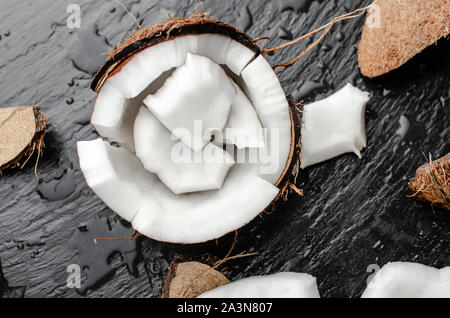 Noix de coco biologique avec des morceaux hlf sur fond noir en ardoise noire. Aliments à forte teneur en gras sain concept. Banque D'Images