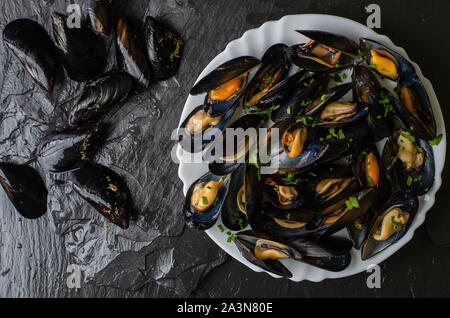 Les moules crues et cuites fraîches sur fond noir en ardoise noire. Concept de fruits de mer. Vue d'en haut Banque D'Images