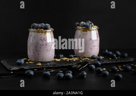 Petit-déjeuner sain concept. Pots de yaourt fait maison avec des bleuets et de l'avoine sur fond noir. Vue de face. Banque D'Images
