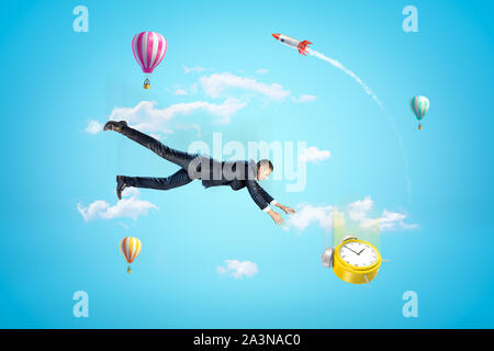Young Woman in blue sky tomber en essayant d'attraper réveil jaune, avec des ballons à air chaud et de lance en arrière-plan. Banque D'Images