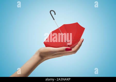 Gros plan du côté de woman's hand holding petit parapluie rouge à l'envers sur sa paume sur fond dégradé bleu clair. Banque D'Images