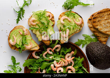 De délicieux plats sains. Toasts à l'avocat, crevettes et salade de roquette sur fond blanc. Haut de la vue, télévision lay. Banque D'Images