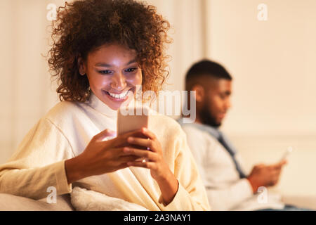 Fille infidèle texting on phone avec copain sur canapé Banque D'Images