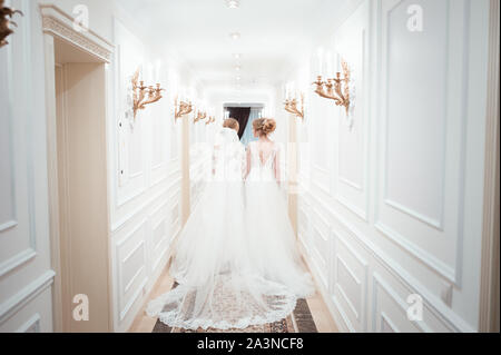 Deux filles en robes de mariage. à pied le long d'un long couloir blanc. rechercher de la colonne vertébrale. girlfriends Banque D'Images