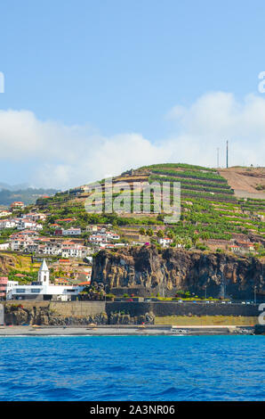 Magnifique petit village de pêcheurs de Camara de Lobos dans l'île de Madère, Portugal photographié dans les eaux de l'océan Atlantique. Ville pittoresque sur une colline par la côte. Destination touristique. Banque D'Images