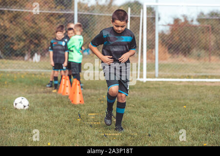 Exercices de soccer : Kid soccer player le jogging et le saut à l'échelle de l'anneau vert marqueur sur gazon artificiel. Matériel pour la classe de formation de football academy. Banque D'Images