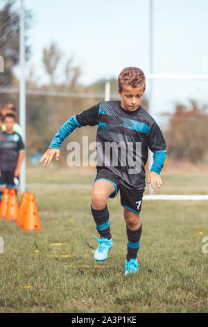 Exercices de soccer : Kid soccer player le jogging et le saut à l'échelle de l'anneau vert marqueur sur gazon artificiel. Matériel pour la classe de formation de football academy. Banque D'Images