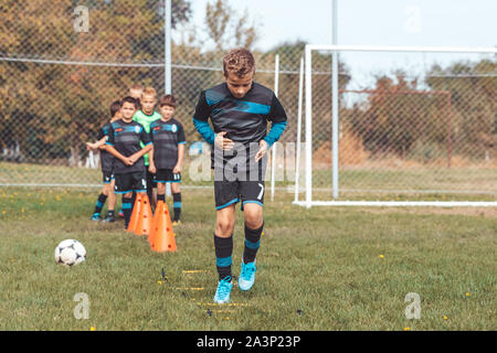 Le joueur de soccer Kid le jogging et le saut à l'échelle anneau marqueur sur gazon artificiel vert. l'équipement pour la classe de formation de football academy. Banque D'Images