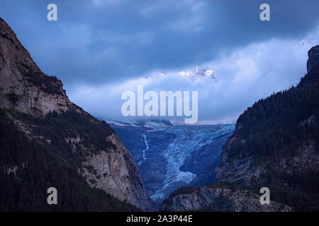 Vue panoramique sur le glacier alpin dans le crépuscule. Sommets enneigés apparaissent derrière les nuages. Ciel couvert. Paysage alpin d'été au crépuscule. Zone de Grindelwald. Banque D'Images