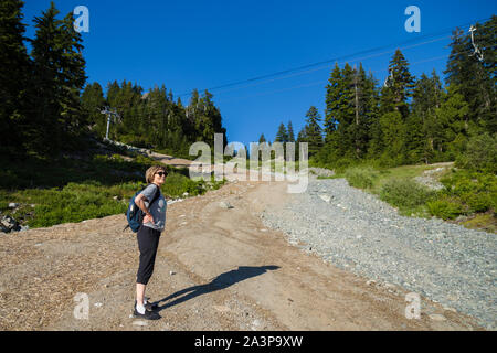 Une femme d'âge moyen marche sur un sentier de randonnée de la forêt de montagne avec une vue sur une ville. Banque D'Images