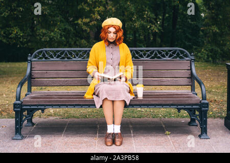 Une belle fille aux cheveux roux avec un curly hairstyle est assis sur un banc de parc Banque D'Images