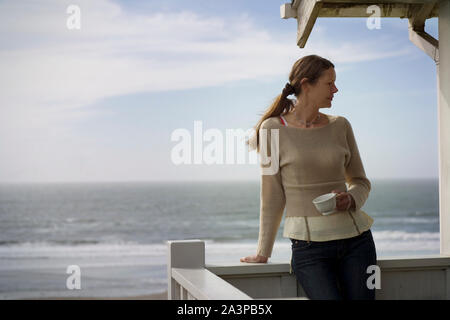 Jeune femme debout avec une tasse de thé sur un balcon par la mer. Banque D'Images