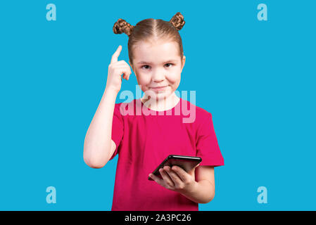 Petite fille avec une expression du visage pensif utilise un smartphone isolé sur un fond bleu. Banque D'Images