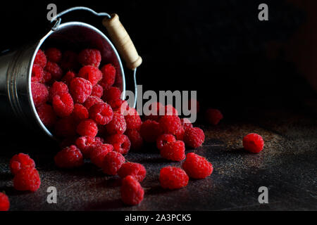 Framboises fraîches dans un petit seau en métal sur fond sombre Banque D'Images