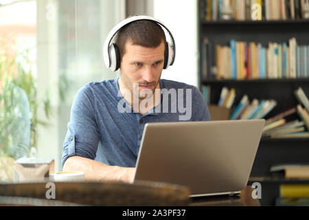 Homme adultes portant des écouteurs à l'aide d'un ordinateur portable e-learning dans un café ou à la maison Banque D'Images