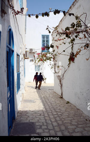 Deux jeunes hommes tunisiens marcher bras dessus, bras dessous dans les rues piétonnes de la Hafsia quart de la médina (vieille ville) de Tunis, Tunisie. Banque D'Images