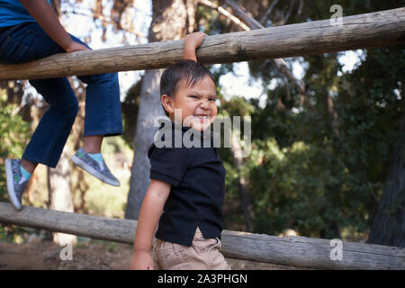 Un heureux petit frère qui veut monter une clôture pour s'asseoir ensemble avec sa sœur aînée dans un parc boisé. Banque D'Images