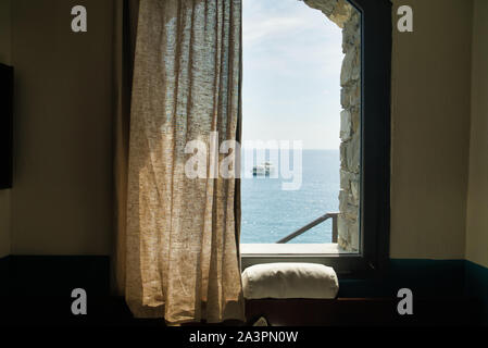 Vue de la fenêtre d'une chambre sur la mer, un bateau à voile au loin, Cinque Terre, Italie Banque D'Images