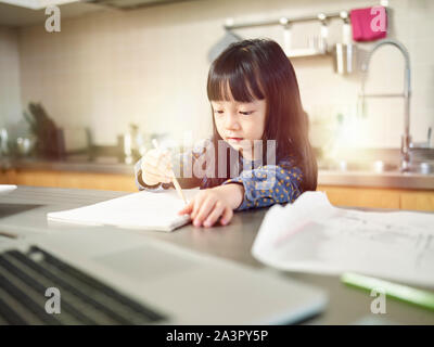 Petite fille asiatique assis au comptoir de la cuisine à la maison faire un dessin. Banque D'Images