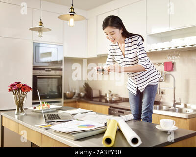 Young Asian woman designer professionnel qui travaille à la maison de prendre une photo de sa conception à l'aide de téléphone mobile. Banque D'Images