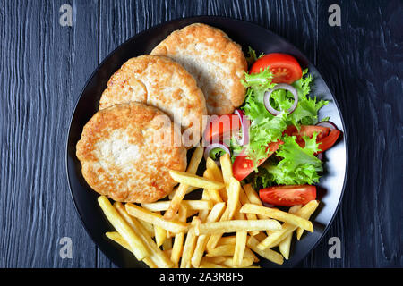 La Turquie fait maison délicieux hamburgers servis avec salade de tomate salade et frites chunky sur une plaque noire sur une table en bois noir, vue de dessus, flatlay Banque D'Images