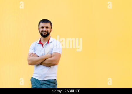 Un jeune et bel homme dans un polo avec une barbe est debout contre un mur jaune. Hipster. Banque D'Images