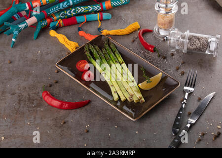 Asperges vertes poêlées avec tomate cerise, citron et piment sur une assiette de service Banque D'Images