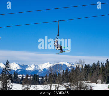 D'un télésiège avec un skieur méconnaissable sur ciel bleu au-dessus des Tatras et une forêt à Bialka ski en Pologne Banque D'Images