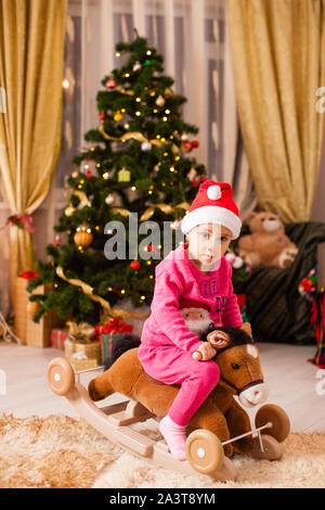 Happy girl riding a horse en face de l'arbre de Noël à la maison. Banque D'Images