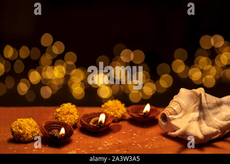 Diwali diya lampes d'argile décorées de fleurs et de shankh brûlant ou brillant sur un fond de bois isolé en noir avec lumières bokeh et copy space Banque D'Images