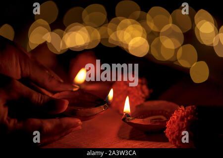 Femme indienne, femme hand holding et d'allumer une lampe à huile en argile ou Diya Indien pendant Diwali festival hindou avec lumières fond flou. Banque D'Images